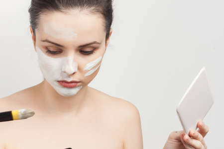 attractive brunette with cream on her face brush in hands applying makeup