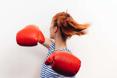 red-haired woman in gloves is engaged in boxing on a light background model aggressionの写真素材