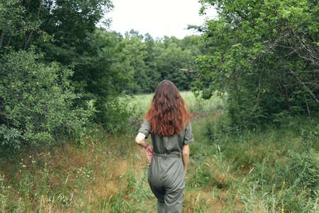 brunette woman in overalls on the meadow back viewの写真素材
