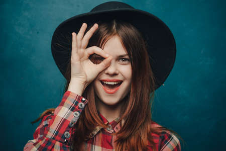 attractive woman with a hat on her head and a plaid shirt gesturing with her hands portrait
