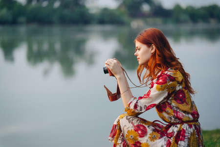 woman in a multicolored dress with a camera in her hands outdoors near the river hobbyの写真素材