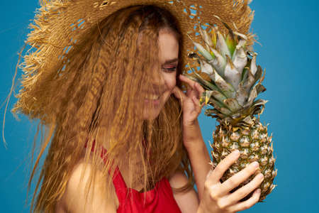 A woman in a straw hat with a pineapple in her hands or is it a fun blue exotic fruits background
