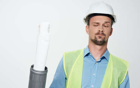 A man builder in a yellow vest and a white helmet with a roll of paper in his hand repairing work