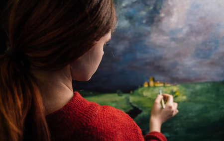a woman paints a picture with bright paints on canvas and a brush in her hand