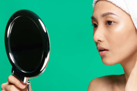 pretty woman mirror on her hands clean skin face close up green backgroundの写真素材