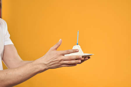 Cake with a candle in a mans hand on a yellow background cropped view Copy Space