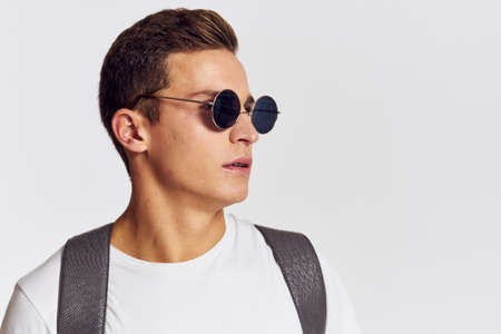 man in sunglasses with a backpack on his back and in a white t-shirt on a light background cropped...