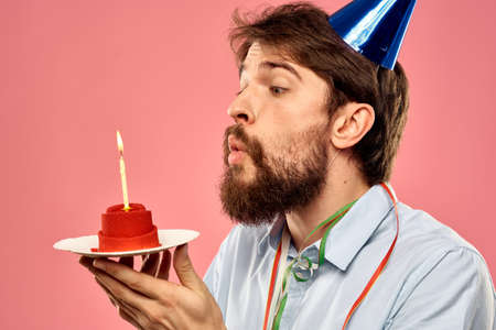 Man with a cake with a candle and a birthday cap on a pink backgroundの写真素材