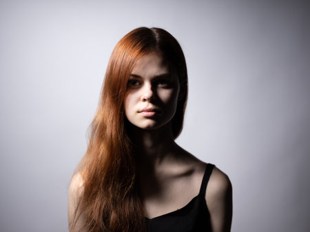 Beautiful woman with red hair in a black dress on a gray background bared shouldersの写真素材