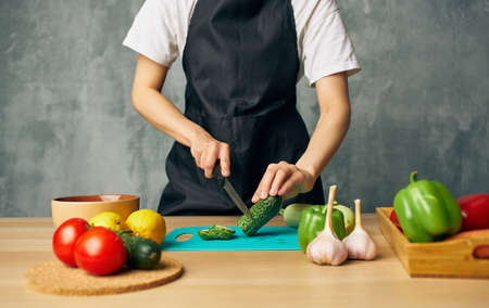 Woman cook black apron slicing vegetables cutting board kitchen cooking foodの写真素材