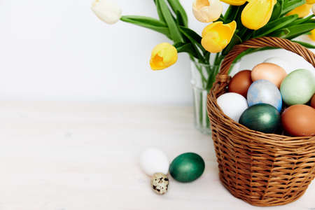Easter holiday colorful eggs in a basket and a bouquet of yellow tulipsの写真素材