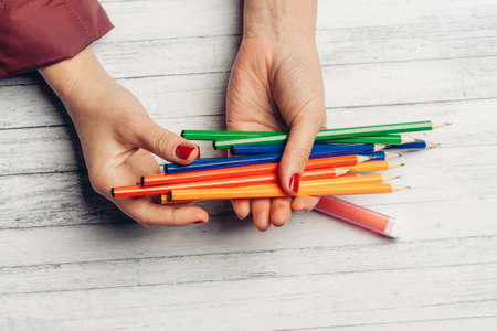 bright colored pencils in female hands wooden background texture gray colorの写真素材