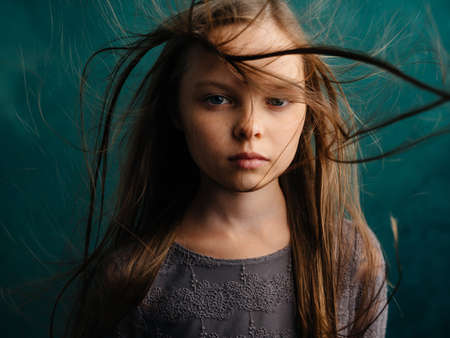 Pretty little girl with disheveled hair on a turquoise backgroundの写真素材