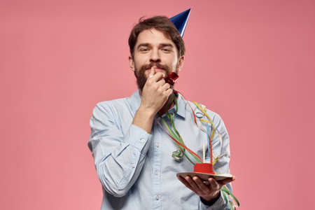 Man with cake in a plate and in a blue shirt on a pink background birthday holidays cropped viewの写真素材