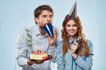 Birthday man woman in party hats on a blue background and cake with candlesの写真素材