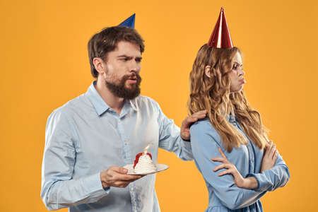 Birthday party man and woman in a cap with a cake on a yellow background cropped view