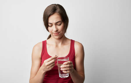 makeup woman in red t-shirt holds glass of water pill medicine health problemsの写真素材