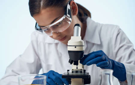 female laboratory assistant with a microscope on the table and glasses on the face liquid in a flaskの写真素材