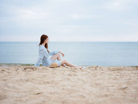 Women on the sand in a sundress near the sea with a hat in handの写真素材