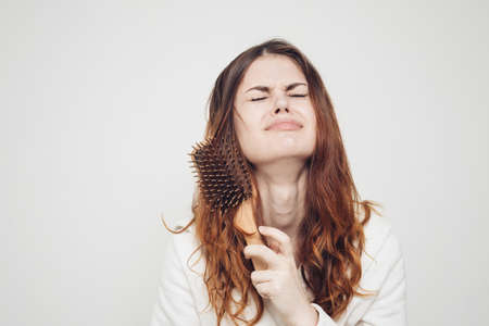 red-haired woman combing tangled curls on a light backgroundの写真素材