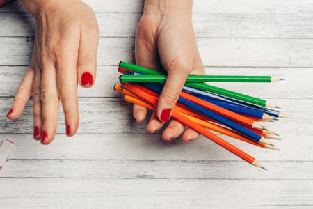 bright colored pencils in woman hands on wooden background cropped view