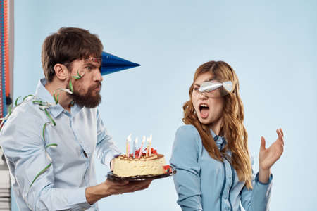 Birthday man woman in party hats on a blue background and cake with candles