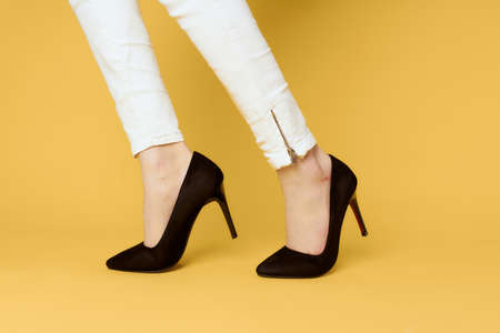 Female legs black shoes fashion attractive look white jeans yellow backgroundの写真素材
