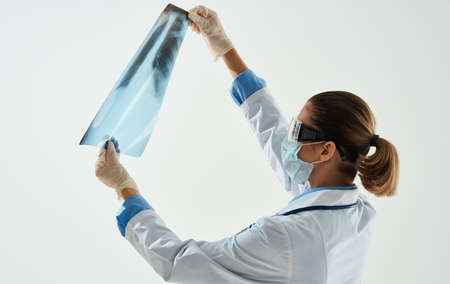 A woman doctor in a medical mask examines an X-ray on a light backgroundの写真素材