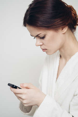 woman with a mobile phone holds a sponge in her hand on a light backgroundの写真素材