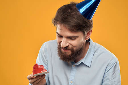a man with a birthday cake in his hands and in a cap on a yellow background on his birthdayの写真素材