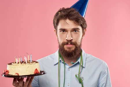 A man in a shirt with a cake in his hands and a festive cap on his head