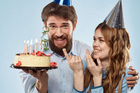 Birthday man woman in party hats on a blue background and cake with candles