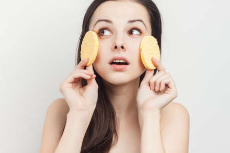 brunette with bare shoulders holds sponges near her faceの写真素材