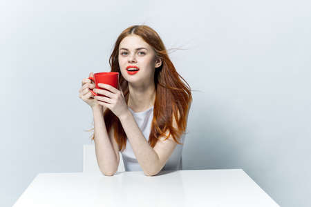 pretty woman holding a red mug in her hand while sitting at the table coffee