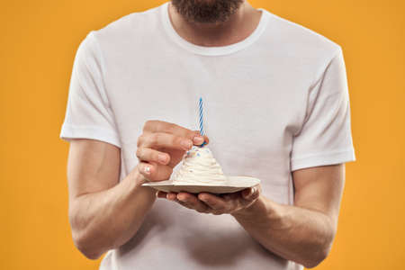 A man with a birthday cake in his hands on a yellow background birthday dessertの写真素材