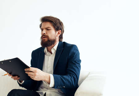 A business man in a suit with documents in his hands on a connected uniform sits on a sofa indoorsの写真素材