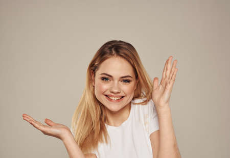 Happy blonde woman gesturing with her hands on a beige background close-up