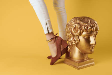 Female feet fashionable shoes elegant style head sculpture yellow background