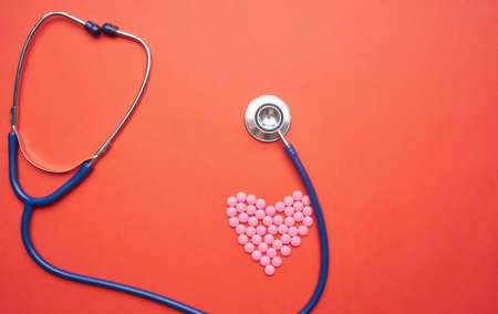 stethoscope and pills in the form of a heart on a red background medicine health vitamins
