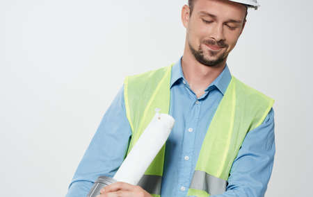A man builder in a yellow vest and a white helmet with a roll of paper in his hand repairing work