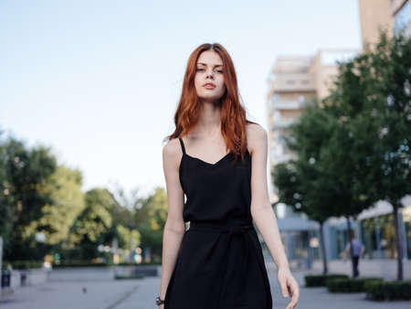 Fashionable Woman in a black dress walks down the street in the park in nature