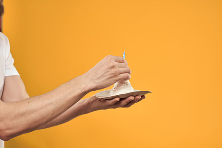 Cake with a candle in a mans hand on a yellow background cropped view Copy Space
