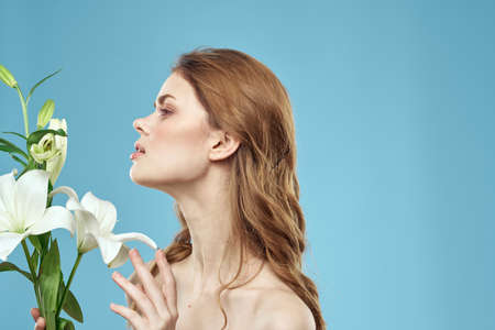 Woman with a bouquet of white flowers on a blue background naked shoulders beautiful faceの写真素材