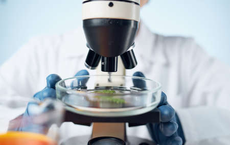 microscope on the table and female laboratory assistant in blue gloves liquid in a flask