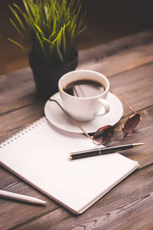 potted flower notepads pens stationery and coffee cup glasses wooden tableの写真素材