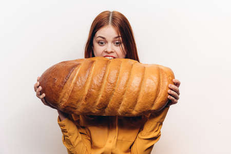 hungry woman with a huge loaf on a light background and a yellow shirt to
