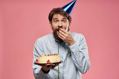 Bearded man with cake on pink background birthday party corporate emotions model lonelinessの写真素材