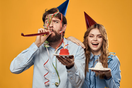 Man and woman at a party in caps and with tinsel cake fun yellow backgroundの写真素材