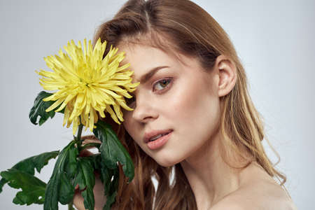 Portrait of a beautiful woman with a yellow flower on a light backgroundの写真素材