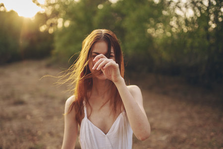 romantic woman in a dress gestures with her hands outdoors near green treesの写真素材